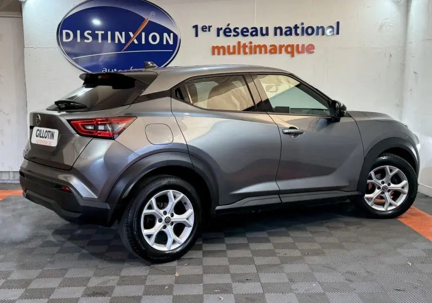 Nissan Juke gris clair vu de profil côté gauche, avec jantes alliage et toit noir en arrière-plan showroom.