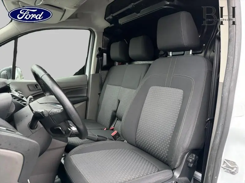Vue intérieure côté conducteur du Ford Transit Connect blanc glacier, montrant les sièges tissu gris et le volant multifonction.