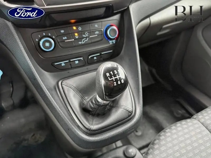 Gros plan sur le levier de vitesses manuel noir et la console centrale du Ford Transit Connect blanc glacier, avec commandes de climatisation.