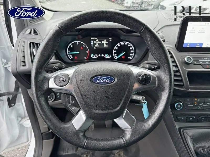 Vue intérieure centrée sur le volant multifonction noir du Ford Transit Connect blanc glacier avec tableau de bord et écran SYNC 3.