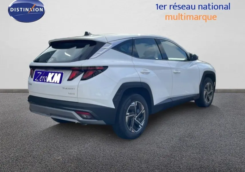 Vue 3/4 arrière droite d'un Hyundai Tucson blanc Atlas hybride avec jantes bi-ton et feux arrière LED distinctifs.