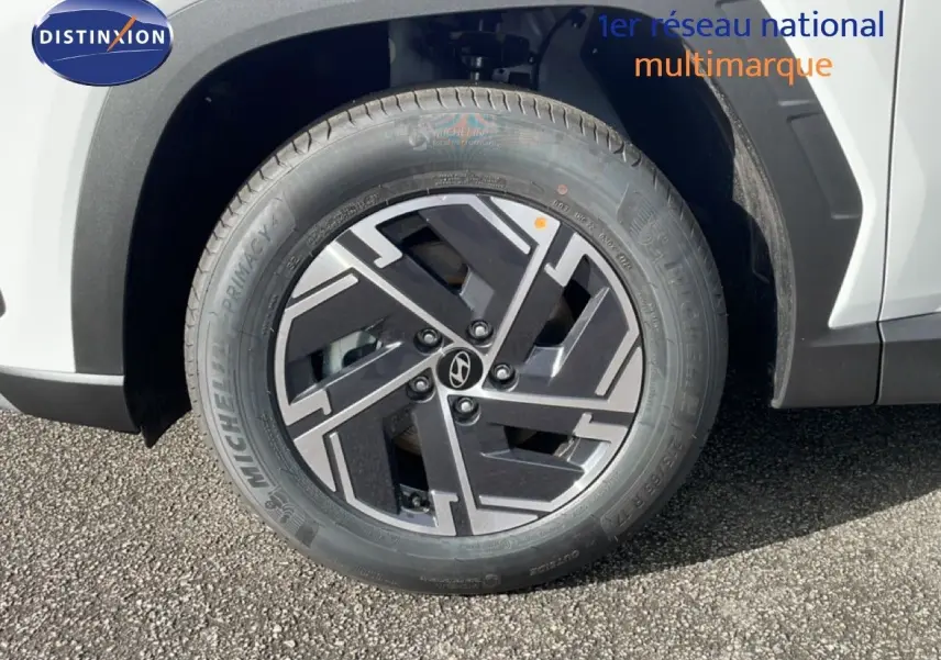 Gros plan sur la roue avant droite du Hyundai Tucson blanc Atlas, mettant en valeur la jante noire et grise au design géométrique.