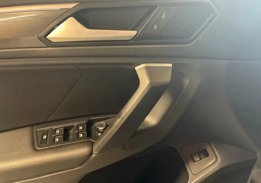Détail de la porte côté conducteur du Volkswagen Tiguan 2020, montrant les commandes de vitres et la poignée intérieure en noir.