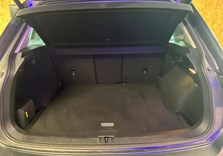 Coffre ouvert d’un Volkswagen Tiguan gris, vue arrière montrant l’espace de chargement vide et la tablette cache-bagages relevée.