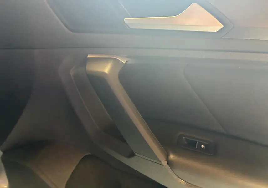 Détail de la porte intérieure côté droit du Volkswagen Tiguan gris, avec poignée angulaire et bouton de verrouillage.