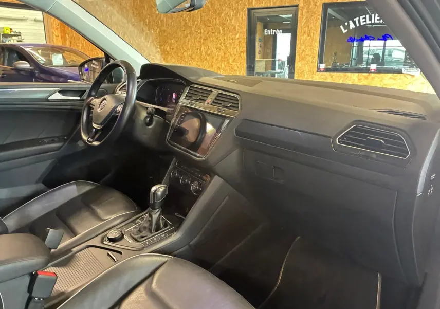 Vue intérieure côté conducteur du Volkswagen Tiguan gris 2020, avec tableau de bord moderne et sellerie cuir noire.