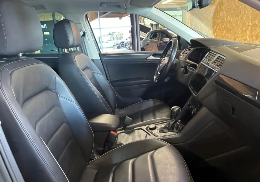 Vue intérieure côté conducteur du Volkswagen Tiguan 2.0 TDI gris, sièges cuir noir et console centrale avec boîte auto.