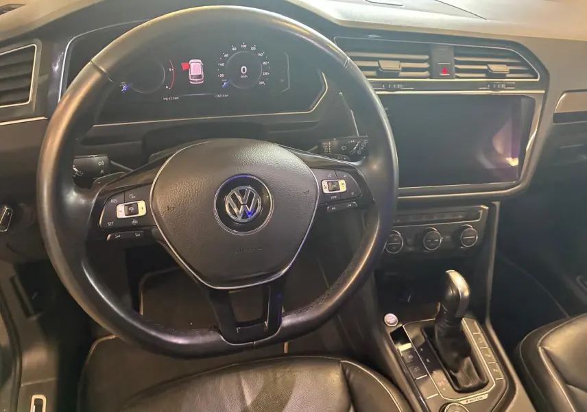 Vue intérieure centrée sur le volant noir et la console centrale d'un Volkswagen Tiguan gris, avec écran tactile éteint.