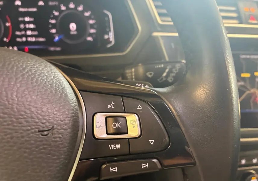 Gros plan sur les commandes du volant noir du Volkswagen Tiguan gris, avec tableau de bord numérique en arrière-plan.