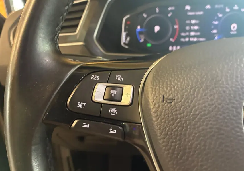 Gros plan sur le volant noir du Volkswagen Tiguan 2020 avec commandes de régulateur de vitesse et tableau de bord numérique flou.
