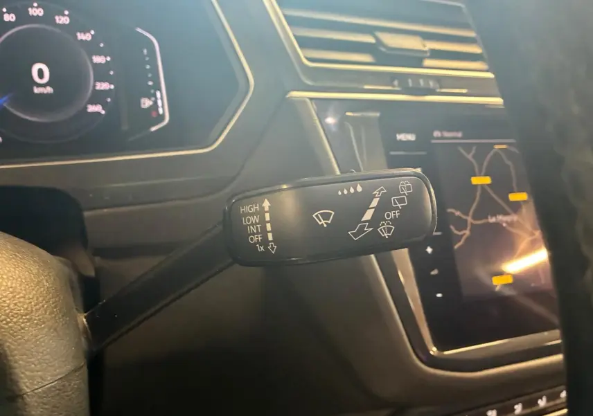Gros plan sur la commande d’essuie-glace à gauche du volant dans l’habitacle noir du Volkswagen Tiguan gris, avec tableau de bord digital et écran GPS.