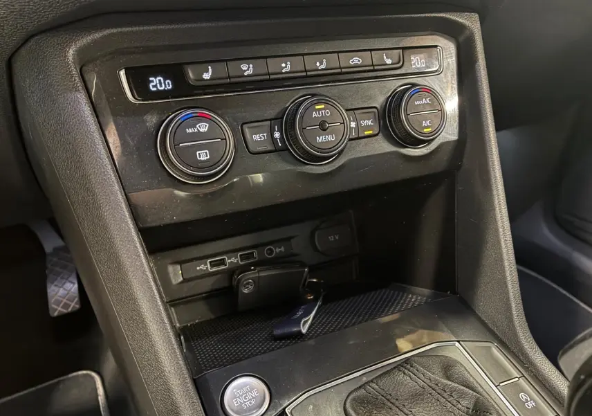 Vue rapprochée de la console centrale noire du Volkswagen Tiguan 2020, montrant les commandes de climatisation et le bouton start/stop.