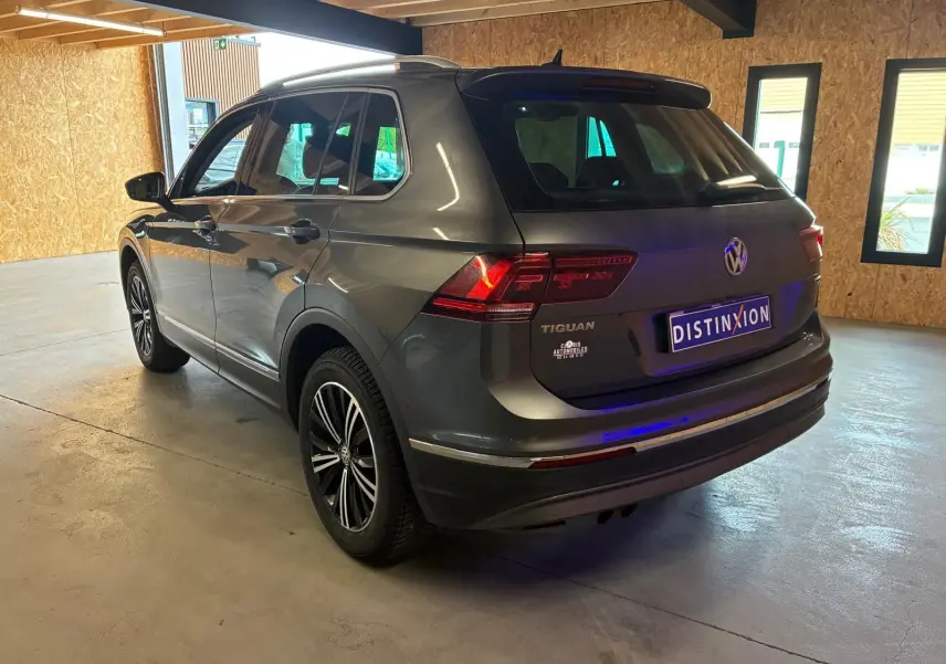 Vue 3/4 arrière droite d'un Volkswagen Tiguan gris stationné en intérieur avec feux arrière allumés et jantes noires.