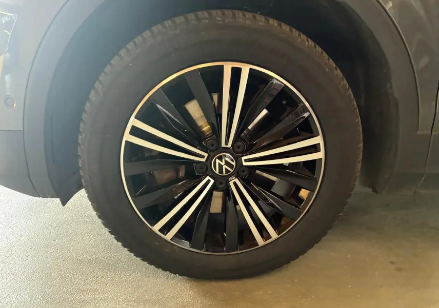 Gros plan sur la roue avant gauche d’un Volkswagen Tiguan gris, mettant en valeur la jante noire et argentée au design moderne.