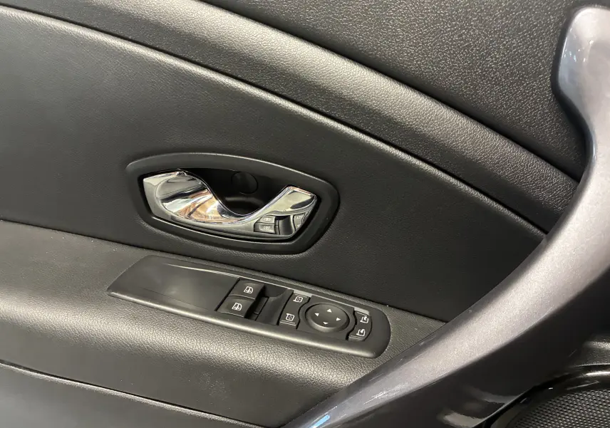 Gros plan sur la poignée intérieure chromée et les commandes électriques des vitres côté conducteur d'une Renault Mégane Coupé noire.