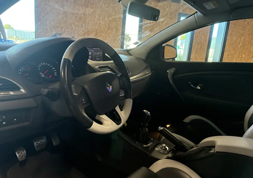 Vue intérieure côté conducteur de la Renault Mégane Coupé 2.0 DCI 165 GT 2014 avec volant cuir bicolore et tableau de bord noir.
