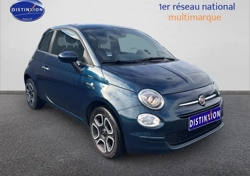 Vue 3/4 avant droite d'une FIAT 500 bleu foncé 2023 avec jantes stylisées et phares allumés.
