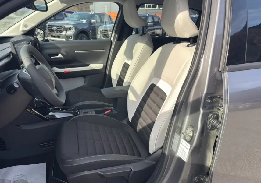 Intérieur avant du Citroën C3 Aircross gris mercury, sièges tissu bicolores noir et beige, volant multifonctions visible.