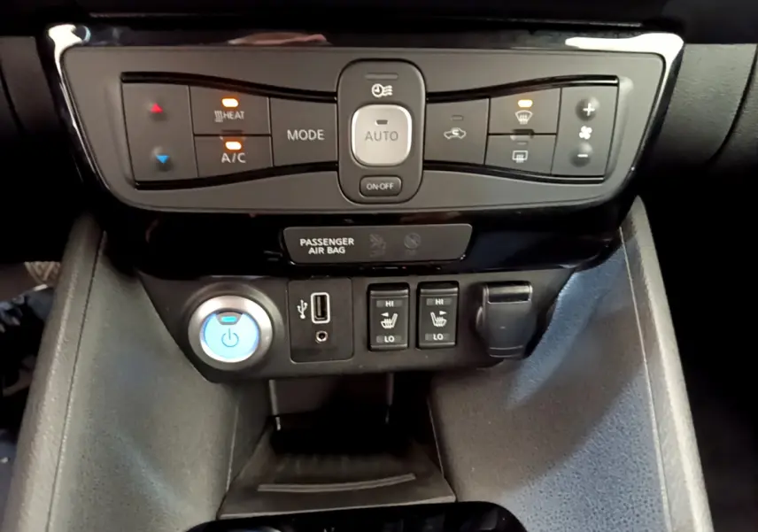 Vue rapprochée du tableau de bord central de la Nissan Leaf blanche 2020, avec commandes climatisation et sièges chauffants.