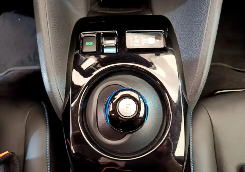 Gros plan sur la molette de boîte automatique noire avec bouton "P" bleu au centre de la console d'une Nissan Leaf blanche.