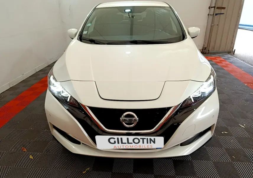 Vue avant d'une Nissan LEAF blanche 62 kWh avec phares LED allumés dans un garage fermé.