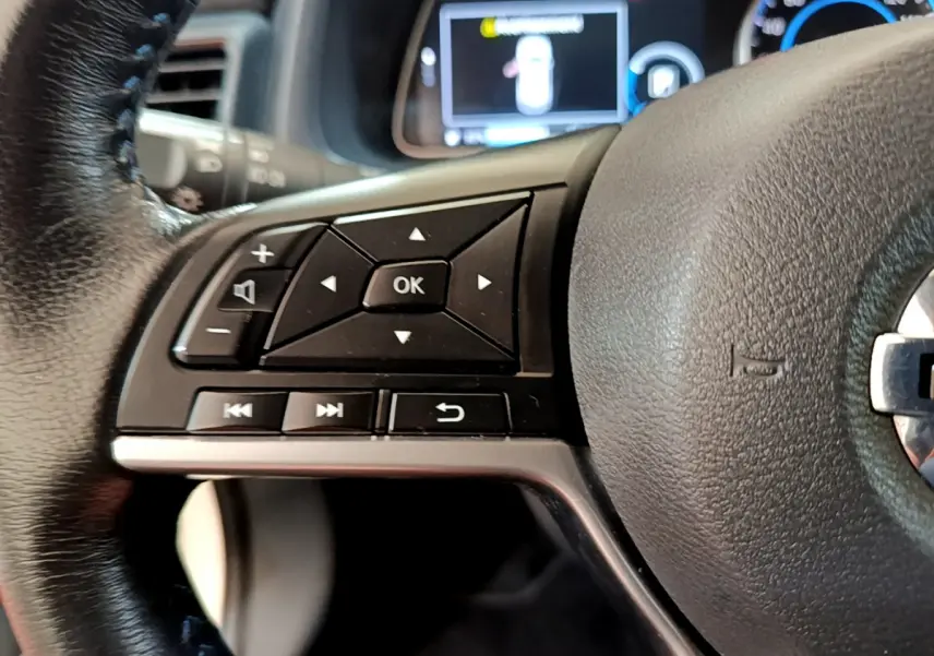 Gros plan sur les commandes gauche du volant cuir de la Nissan LEAF 62 kWh 2020 avec affichage numérique en arrière-plan.