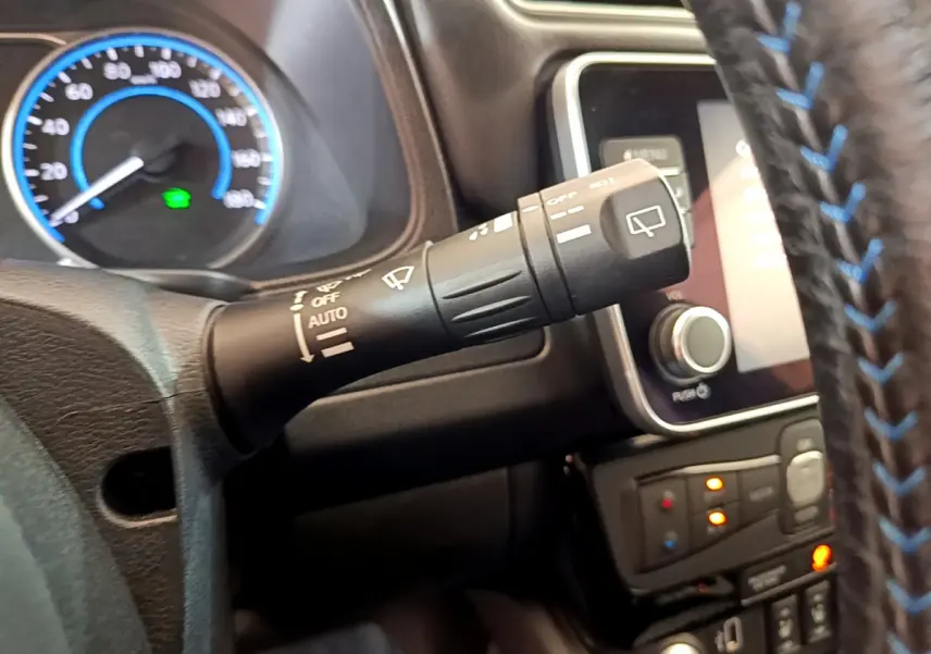 Gros plan sur la commande d’essuie-glace à gauche du volant cuir noir avec surpiqûres bleues du Nissan Leaf blanc 2020.