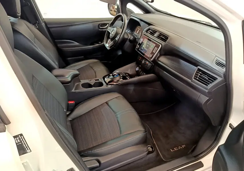 Intérieur avant droit de la Nissan Leaf blanche 2020, sièges noirs, tableau de bord avec écran tactile et volant cuir.
