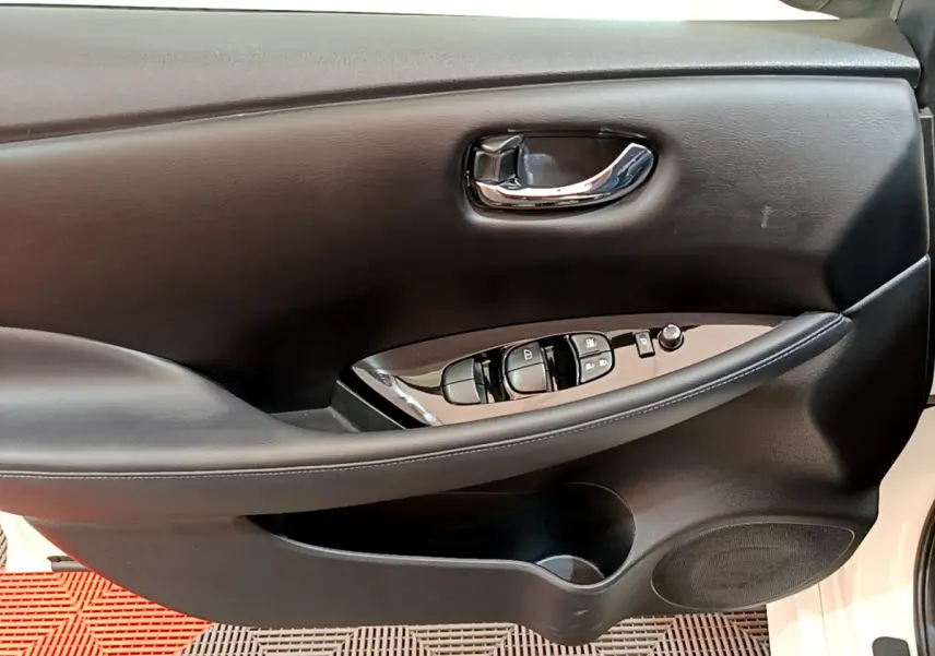 Gros plan sur la porte intérieure côté conducteur noire du Nissan Leaf blanc, avec commandes électriques et poignée chromée.