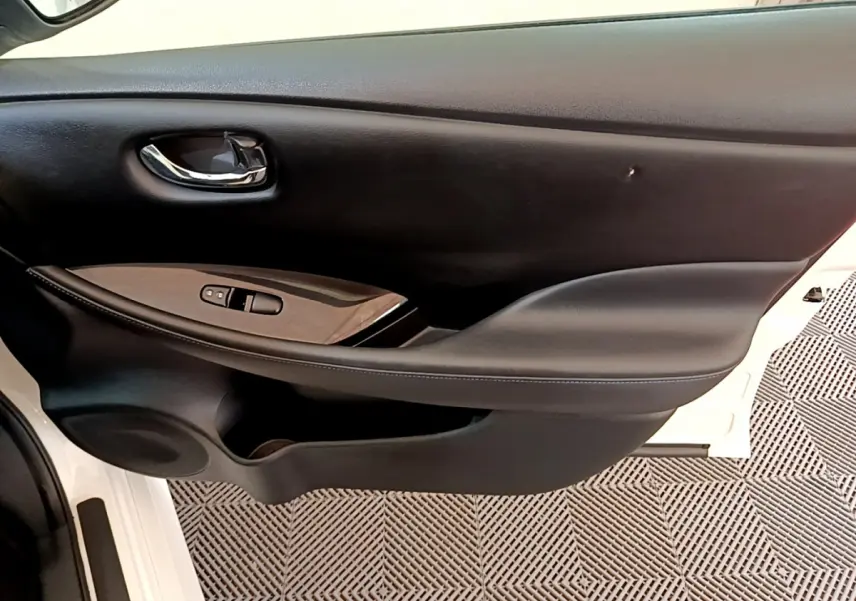 Porte intérieure côté gauche de Nissan Leaf blanche 2020, avec poignée chrome et commandes de vitres noires.