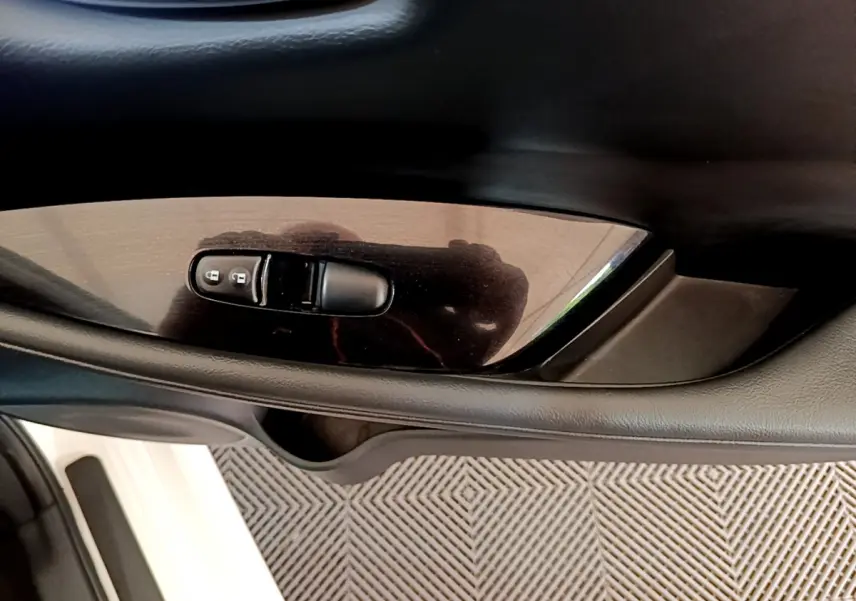 Gros plan sur la commande de verrouillage des portes côté conducteur d'une Nissan Leaf blanche, intérieur noir.