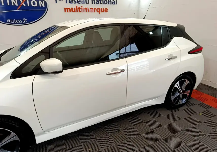 Profil côté gauche d'une Nissan Leaf blanche 2020 avec toit noir et jantes alliage en intérieur showroom.