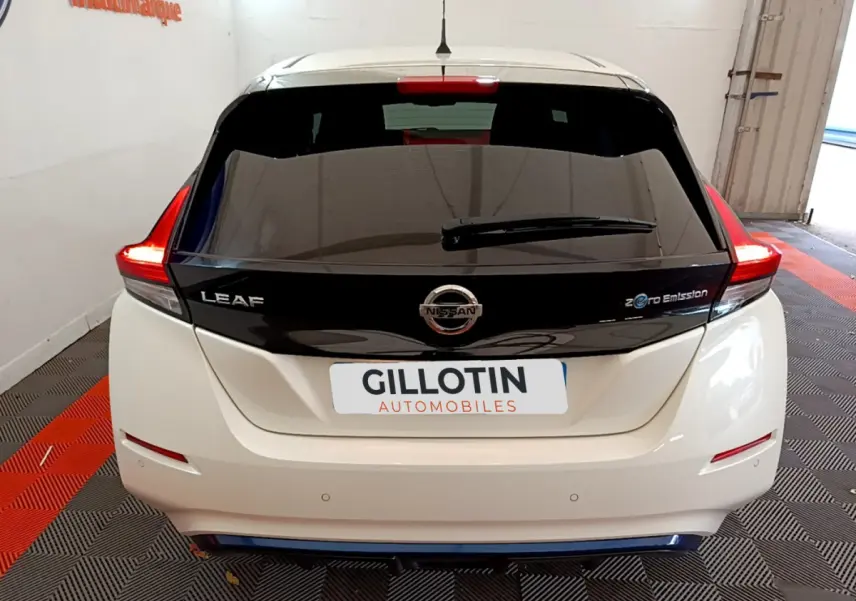 Vue arrière d'une Nissan Leaf blanche avec hayon noir brillant et feux arrière LED allumés dans un garage.