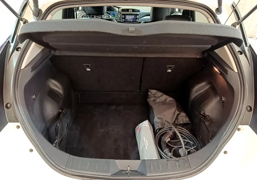 Coffre ouvert vue arrière d'une Nissan Leaf blanche 2020, avec câbles de recharge et trousse de secours visibles.