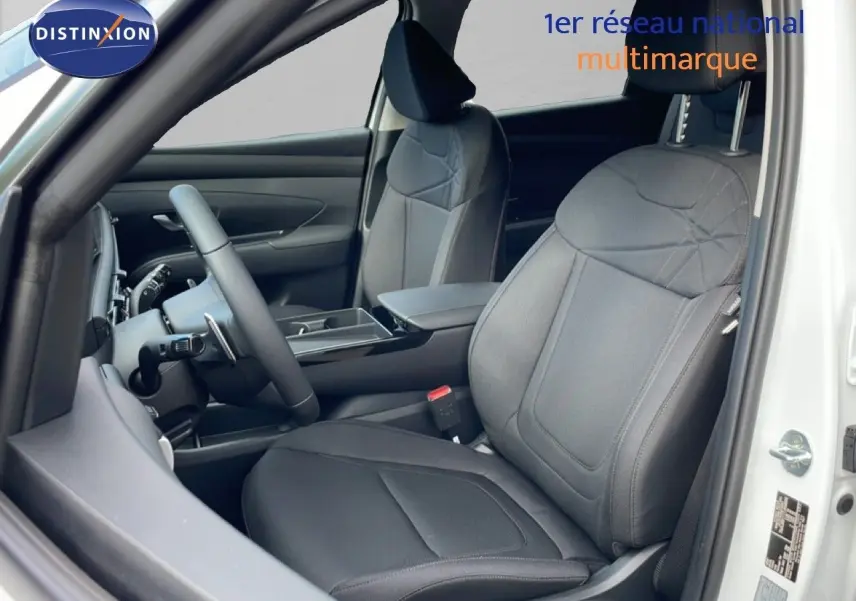 Vue intérieure côté conducteur du Hyundai Tucson blanc Atlas 2026, sièges tissu noir et tableau de bord moderne.