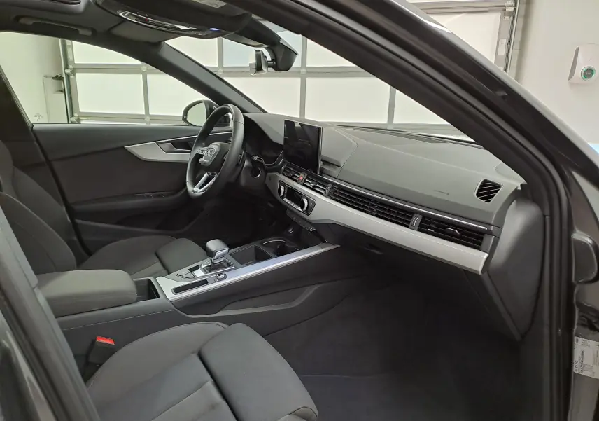 Intérieur de l'Audi A4 Avant 40 TDI 2024 vu côté conducteur, tableau de bord moderne avec écran central et sièges noirs.