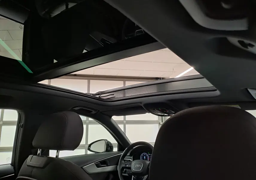 Vue intérieure de l'Audi A4 Avant 2024 avec toit panoramique ouvert et sièges avant noirs.