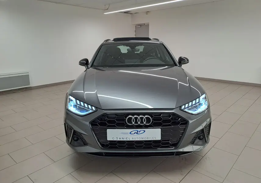 Audi A4 Avant 40 TDI gris Daytona vue de face en intérieur avec phares LED allumés et calandre noire S line.