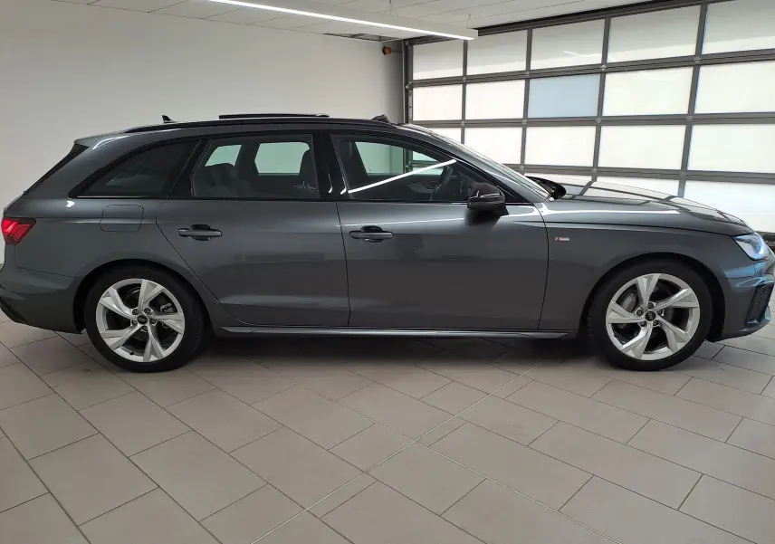 Profil droit d'une Audi A4 Avant 40 TDI gris Daytona avec toit ouvrant panoramique et jantes 18 pouces en intérieur showroom.