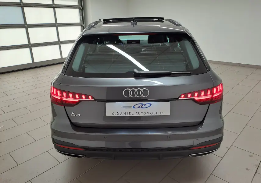 Vue arrière d'une Audi A4 Avant 40 TDI gris Daytona avec feux allumés et toit panoramique en intérieur showroom.