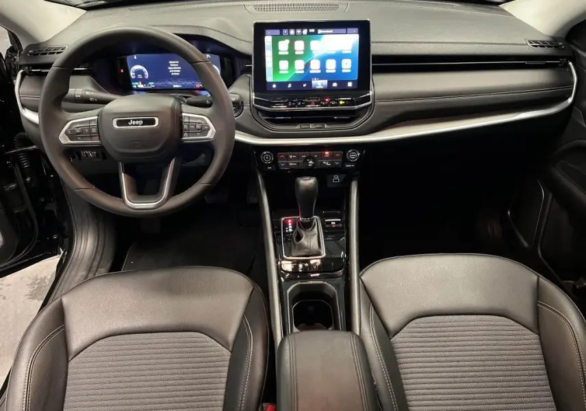 Vue intérieure frontale du Jeep Compass 2024 noir, avec tableau de bord numérique et écran tactile central lumineux.