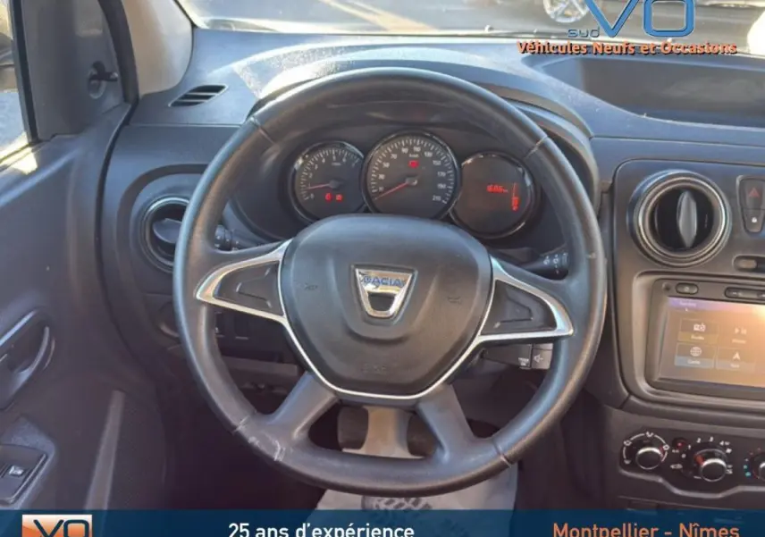 Vue centrée sur le volant et le tableau de bord noir du Dacia Lodgy blanc, avec commandes et écran tactile visibles.