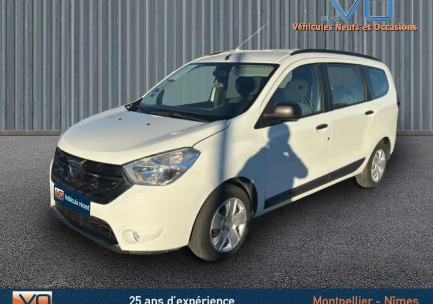 Dacia Lodgy blanc en 3/4 avant droit avec barres de toit, sur fond gris industriel, photo extérieure lumineuse.