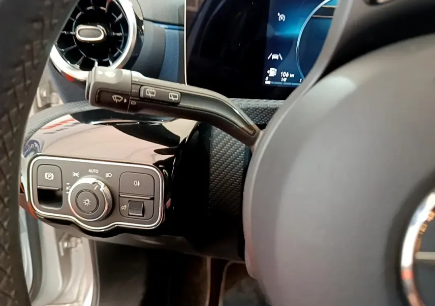 Gros plan sur le tableau de bord côté gauche d'une Mercedes Classe A gris clair, avec commandes d'éclairage et volant partiel visible.