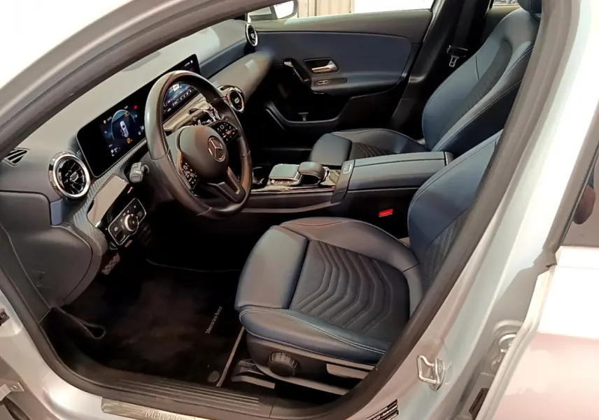 Intérieur côté conducteur d'une Mercedes Classe A gris clair, avec tableau de bord numérique et sièges en cuir noir.