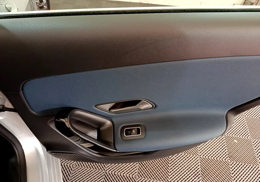 Gros plan sur la porte côté gauche gris clair de la Mercedes Classe A 180 d Business Line avec insert bleu et poignée noire.