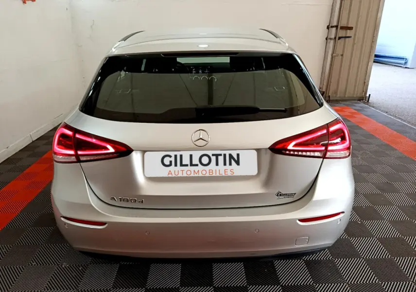 Vue arrière d'une Mercedes Classe A 180 d Business Line gris clair avec feux LED allumés en intérieur showroom.