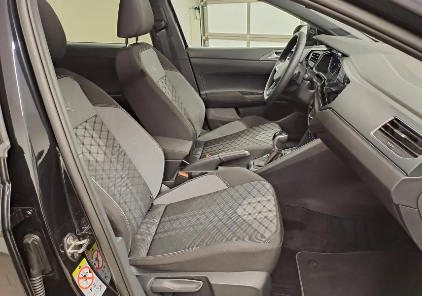 Vue intérieure côté gauche du Volkswagen Taigo 1.5 TSI R-Line 2025, sièges sport gris à motifs et volant cuir multifonctions.