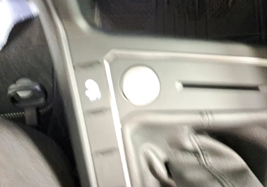 Gros plan sur la console centrale noire avec commande de frein à main cuir et bouton de fonction dans un Volkswagen Taigo noir.