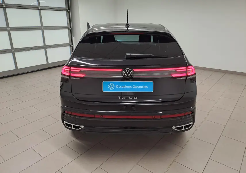 Vue arrière d'un Volkswagen Taigo noir intense nacré avec feux arrière LED allumés et double sortie d'échappement intégrée.